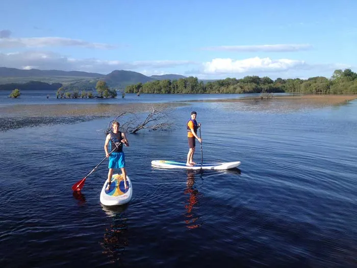 Two people on stand-up paddleboards on dark blue water, with a wooded shore behind