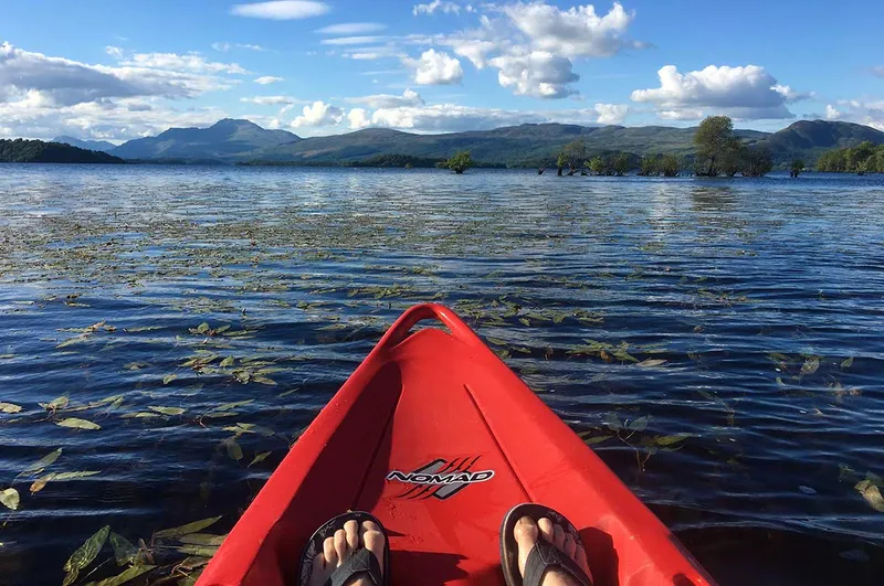 The red bow of a kayak on rippled water, with hills across Loch Lomond