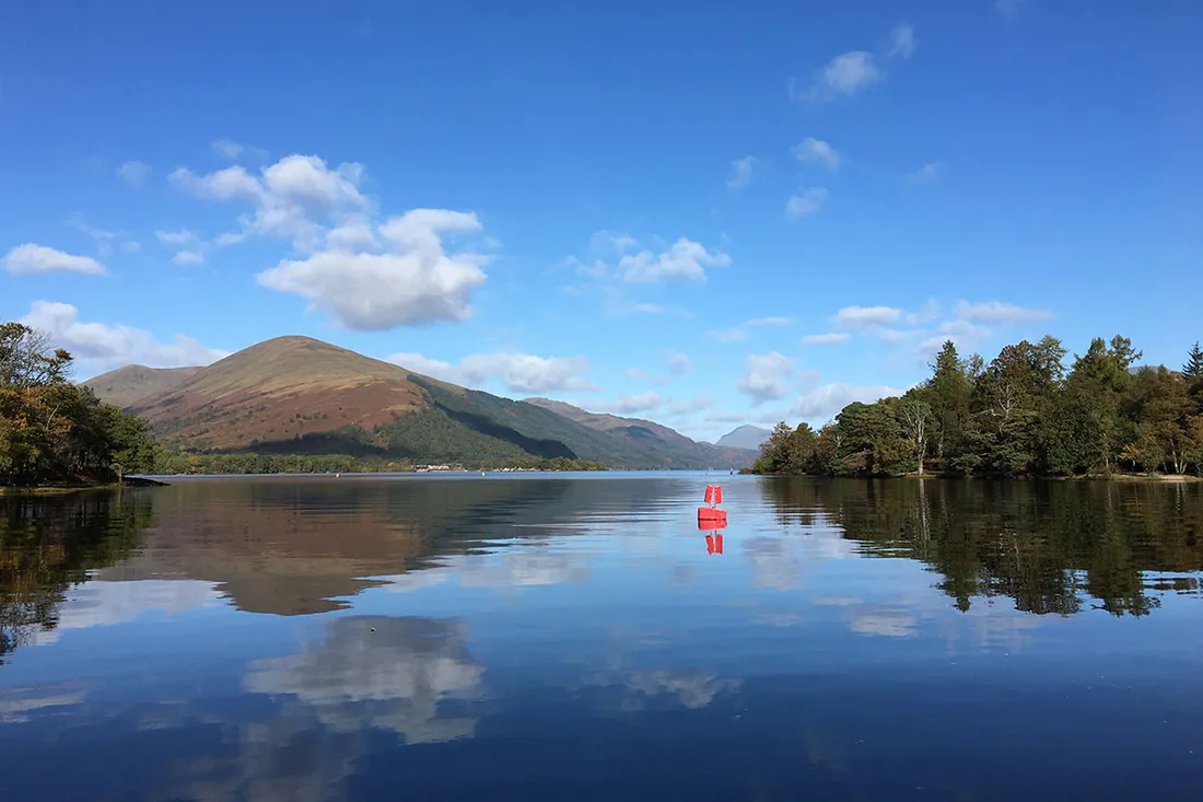Calm water on Loch Lomond with a hill reflected in it