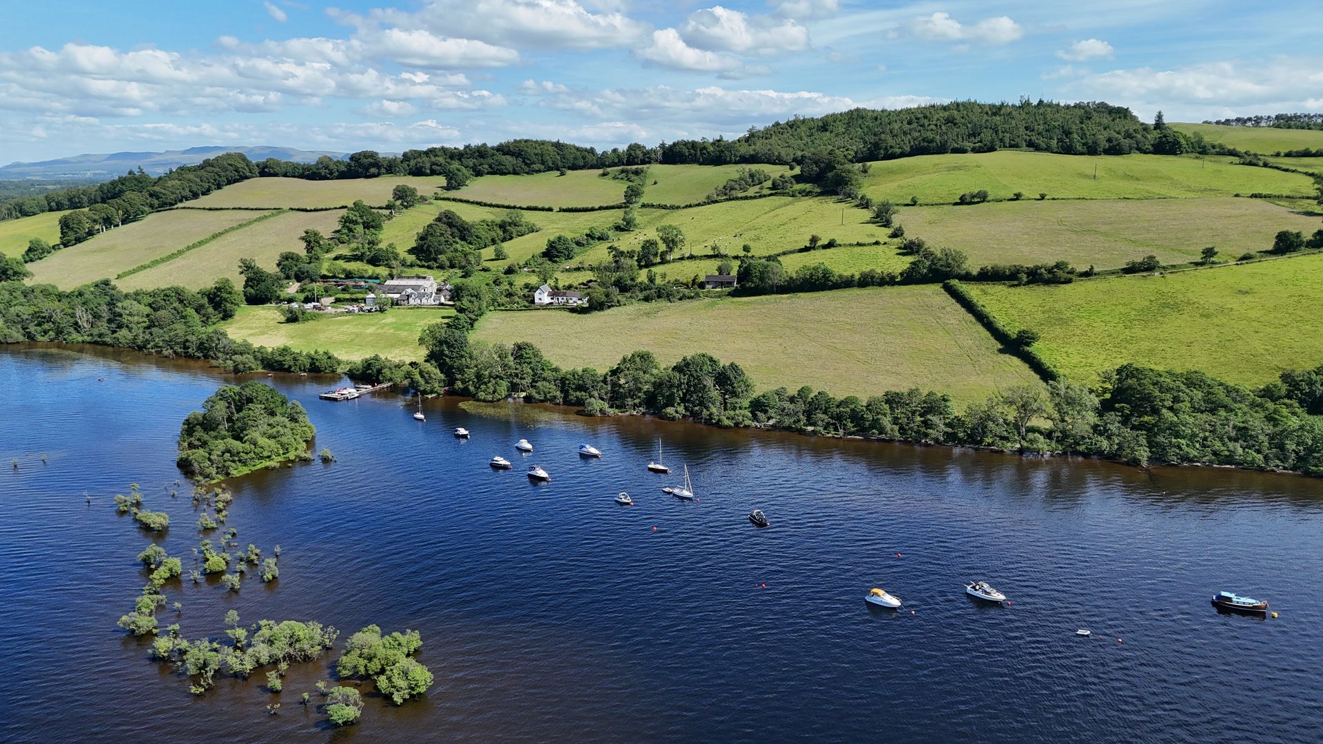 A drone view of Portnellan Bay, with the pier, moored boats and the farm above the water