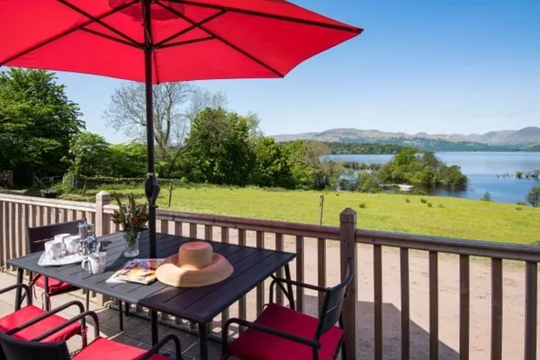 A table and chairs under a red parasol on the front deck, with the loch beyond