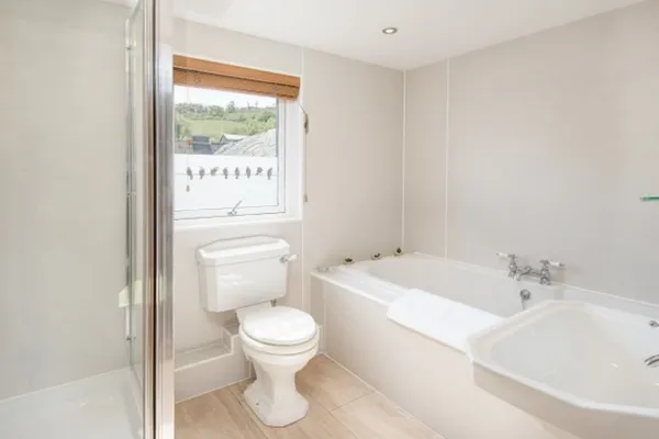 A bathroom with a bath, a toilet and a glass shower screen