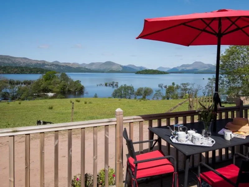 The deck of The Old Farmhouse with a table and chairs looking out over Loch Lomond
