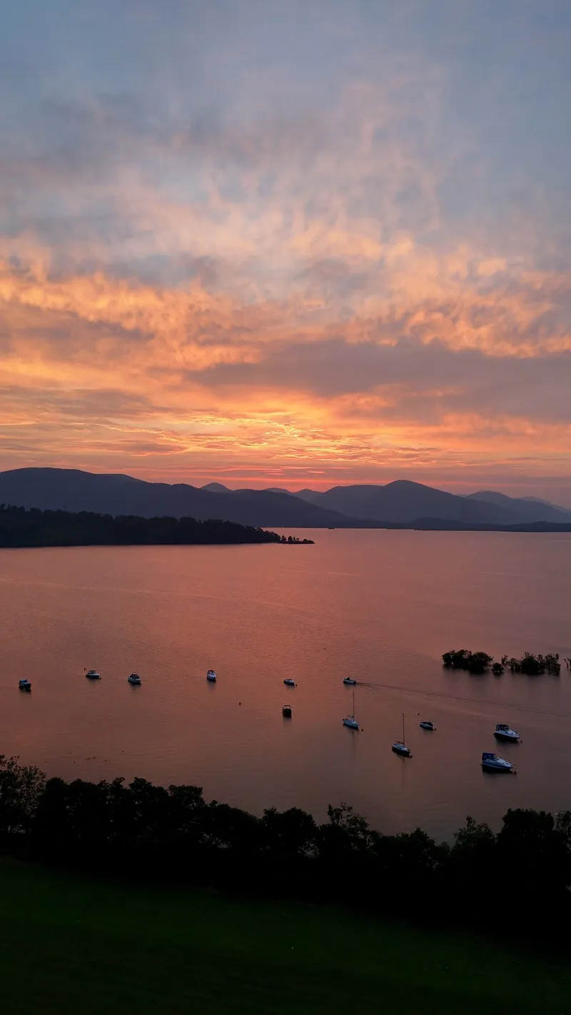 Sunset over Portnellan Bay, with an orange sky above dark hills and small boats at their moorings on calm water